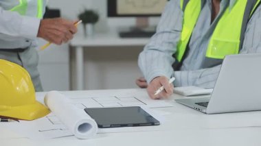 Mühendis ve mimar masanın üstünde bir inşaat planıyla el sıkışıyor.