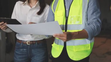 Üniformalı genç bir mühendis elinde planlar ve ofisindeki belgeleri kontrol ediyor.