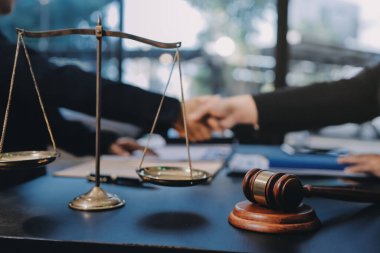 Hukuki bir duruşma sırasında ön planda adalet ve tokmak ile anlaşmaya varan iki avukat el sıkışıyor.