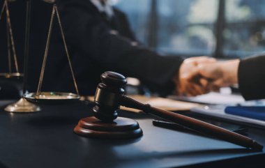 Hukuki bir duruşma sırasında ön planda adalet ve tokmak ile anlaşmaya varan iki avukat el sıkışıyor.