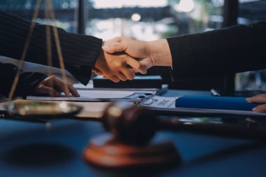 Hukuki bir duruşma sırasında ön planda adalet ve tokmak ile anlaşmaya varan iki avukat el sıkışıyor.