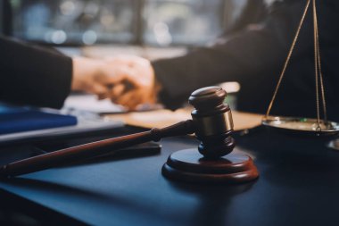 Hukuki bir duruşma sırasında ön planda adalet ve tokmak ile anlaşmaya varan iki avukat el sıkışıyor.