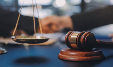 Hukuki bir duruşma sırasında ön planda adalet ve tokmak ile anlaşmaya varan iki avukat el sıkışıyor.