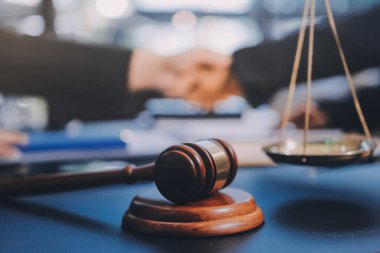 Hukuki bir duruşma sırasında ön planda adalet ve tokmak ile anlaşmaya varan iki avukat el sıkışıyor.