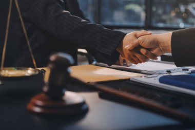 Hukuki bir duruşma sırasında ön planda adalet ve tokmak ile anlaşmaya varan iki avukat el sıkışıyor.