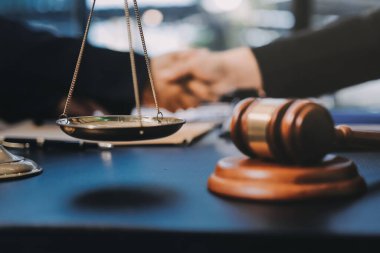 Hukuki bir duruşma sırasında ön planda adalet ve tokmak ile anlaşmaya varan iki avukat el sıkışıyor.