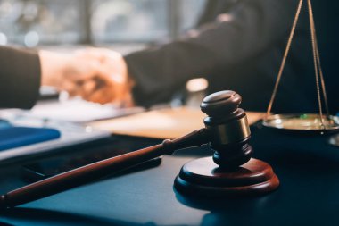 Hukuki bir duruşma sırasında ön planda adalet ve tokmak ile anlaşmaya varan iki avukat el sıkışıyor.