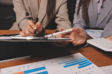 Group of confident business people point to graphs and charts to analyze market data, balance sheet, account, net profit to plan new sales strategies to increase production capacity.