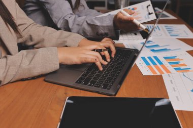 Group of confident business people point to graphs and charts to analyze market data, balance sheet, account, net profit to plan new sales strategies to increase production capacity.