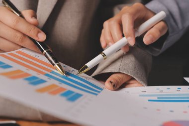 Group of confident business people point to graphs and charts to analyze market data, balance sheet, account, net profit to plan new sales strategies to increase production capacity.