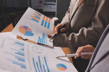 Group of confident business people point to graphs and charts to analyze market data, balance sheet, account, net profit to plan new sales strategies to increase production capacity.