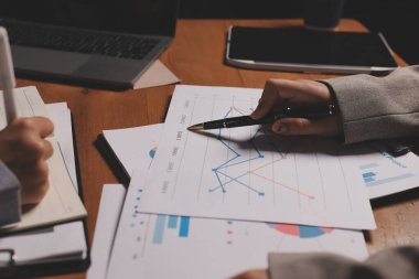 Group of confident business people point to graphs and charts to analyze market data, balance sheet, account, net profit to plan new sales strategies to increase production capacity.