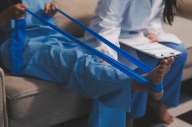 Kendine güvenen fizyoterapist, hastanın bacağını klinik odasında gerdirerek direnç bandı kullanmasına yardım ediyor..