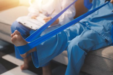 Kendine güvenen fizyoterapist, hastanın bacağını klinik odasında gerdirerek direnç bandı kullanmasına yardım ediyor..