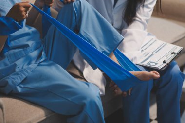 Kendine güvenen fizyoterapist, hastanın bacağını klinik odasında gerdirerek direnç bandı kullanmasına yardım ediyor..