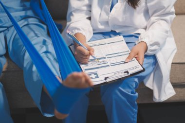 Kendine güvenen fizyoterapist, hastanın bacağını klinik odasında gerdirerek direnç bandı kullanmasına yardım ediyor..