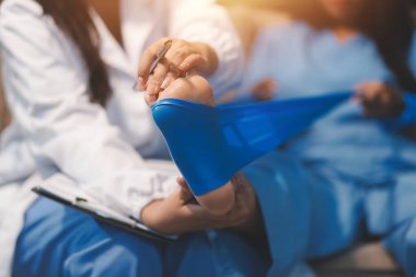 Kendine güvenen fizyoterapist, hastanın bacağını klinik odasında gerdirerek direnç bandı kullanmasına yardım ediyor..