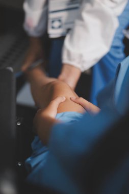 Kadın bir doktor, eklem iltihabı nedeniyle diz ağrısı olan yaşlı bir hastayı muayene eder. Hastaya iyileşme sürecinde yardım ediliyor, ağrı yönetimi ve hareket kabiliyetinin iyileştirilmesi üzerinde duruluyor..