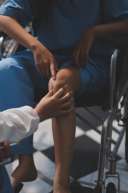 Kadın bir doktor, eklem iltihabı nedeniyle diz ağrısı olan yaşlı bir hastayı muayene eder. Hastaya iyileşme sürecinde yardım ediliyor, ağrı yönetimi ve hareket kabiliyetinin iyileştirilmesi üzerinde duruluyor..