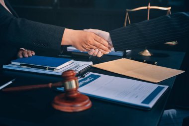 Hukuki bir duruşma sırasında ön planda adalet ve tokmak ile anlaşmaya varan iki avukat el sıkışıyor.