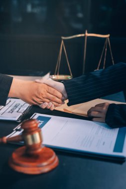 Hukuki bir duruşma sırasında ön planda adalet ve tokmak ile anlaşmaya varan iki avukat el sıkışıyor.