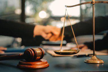 Hukuki bir duruşma sırasında ön planda adalet ve tokmak ile anlaşmaya varan iki avukat el sıkışıyor.