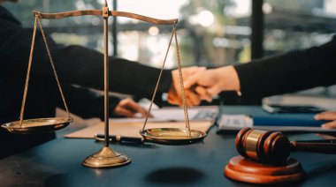 Hukuki bir duruşma sırasında ön planda adalet ve tokmak ile anlaşmaya varan iki avukat el sıkışıyor.