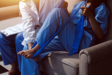 Kendine güvenen fizyoterapist, hastanın bacağını klinik odasında gerdirerek direnç bandı kullanmasına yardım ediyor..