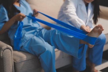 Kendine güvenen fizyoterapist, hastanın bacağını klinik odasında gerdirerek direnç bandı kullanmasına yardım ediyor..