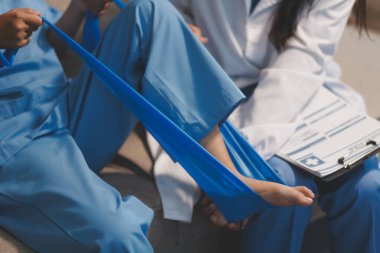 Kendine güvenen fizyoterapist, hastanın bacağını klinik odasında gerdirerek direnç bandı kullanmasına yardım ediyor..