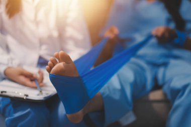 Kendine güvenen fizyoterapist, hastanın bacağını klinik odasında gerdirerek direnç bandı kullanmasına yardım ediyor..