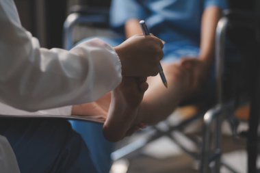 Kadın bir doktor, eklem iltihabı nedeniyle diz ağrısı olan yaşlı bir hastayı muayene eder. Hastaya iyileşme sürecinde yardım ediliyor, ağrı yönetimi ve hareket kabiliyetinin iyileştirilmesi üzerinde duruluyor..