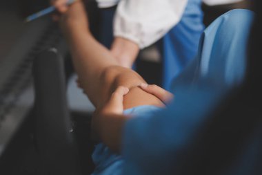 Kadın bir doktor, eklem iltihabı nedeniyle diz ağrısı olan yaşlı bir hastayı muayene eder. Hastaya iyileşme sürecinde yardım ediliyor, ağrı yönetimi ve hareket kabiliyetinin iyileştirilmesi üzerinde duruluyor..