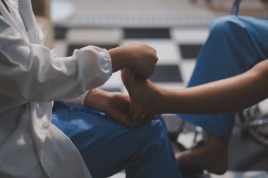 Kadın bir doktor, eklem iltihabı nedeniyle diz ağrısı olan yaşlı bir hastayı muayene eder. Hastaya iyileşme sürecinde yardım ediliyor, ağrı yönetimi ve hareket kabiliyetinin iyileştirilmesi üzerinde duruluyor..