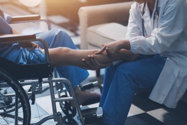 Kadın bir doktor, eklem iltihabı nedeniyle diz ağrısı olan yaşlı bir hastayı muayene eder. Hastaya iyileşme sürecinde yardım ediliyor, ağrı yönetimi ve hareket kabiliyetinin iyileştirilmesi üzerinde duruluyor..