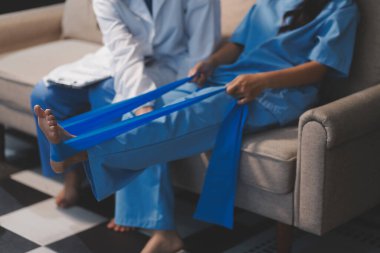 Kendine güvenen fizyoterapist, hastanın bacağını klinik odasında gerdirerek direnç bandı kullanmasına yardım ediyor..