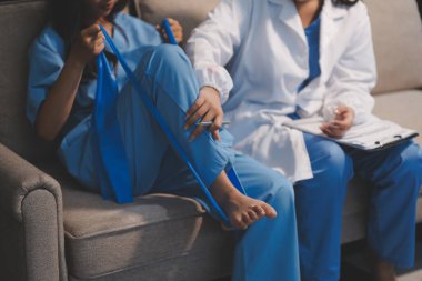 Kendine güvenen fizyoterapist, hastanın bacağını klinik odasında gerdirerek direnç bandı kullanmasına yardım ediyor..