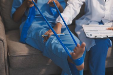 Kendine güvenen fizyoterapist, hastanın bacağını klinik odasında gerdirerek direnç bandı kullanmasına yardım ediyor..