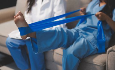 Kendine güvenen fizyoterapist, hastanın bacağını klinik odasında gerdirerek direnç bandı kullanmasına yardım ediyor..