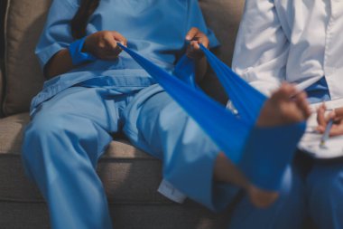 Kendine güvenen fizyoterapist, hastanın bacağını klinik odasında gerdirerek direnç bandı kullanmasına yardım ediyor..