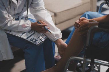 Kadın bir doktor, eklem iltihabı nedeniyle diz ağrısı olan yaşlı bir hastayı muayene eder. Hastaya iyileşme sürecinde yardım ediliyor, ağrı yönetimi ve hareket kabiliyetinin iyileştirilmesi üzerinde duruluyor..