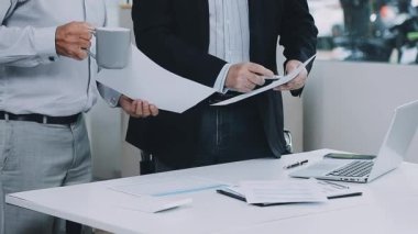 Takım elbiseli ve gömlekli bir iş adamı ofiste doküman ve bilgisayarla çalışıyor..