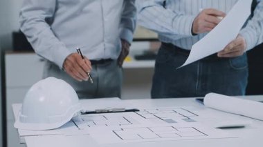 Beyaz kasklı bir erkek mühendis, mimar, beyaz bir iz ve binanın arka planında beyaz bir plan. konsept,