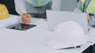 İnşaat mühendisi ya da mimar mühendisi ofiste dizüstü bilgisayarla ya da miğferli, miğferli, planlı, masa üzerinde mühendislik konsepti olan inşaat sahasında çalışıyor.