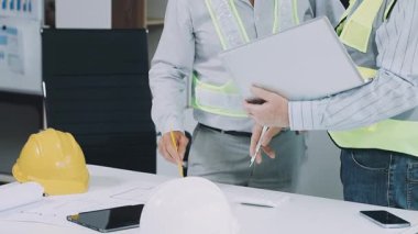 Miğferli ve koruyucu yelekli erkek mühendis inşaat alanında yeni planları tartışıyor.