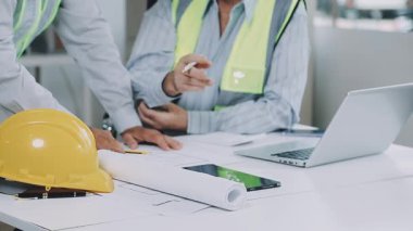 Ofiste güvenlik kaskında planları ve tablet bilgisayarı olan bir mühendis.