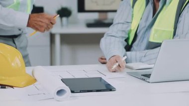 Miğferli mimar ya da mimar mühendis ofiste planlar üzerinde çalışıyor..