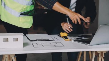 Genç adam dizüstü bilgisayarla ve inşaat planıyla çalışıyor..