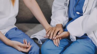 Üniformalı genç bayan doktor hastasının elini tutuyor, hastanede masada oturuyor. tıbbi servis kavramı.