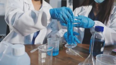 Koruyucu gözlüklü kadın bilim adamı laboratuarda matarayla deney yapıyor.